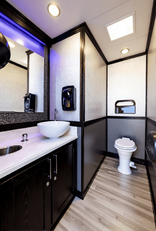 Modern portable restroom interior featuring a vessel sink, dark cabinetry, and a white toilet.