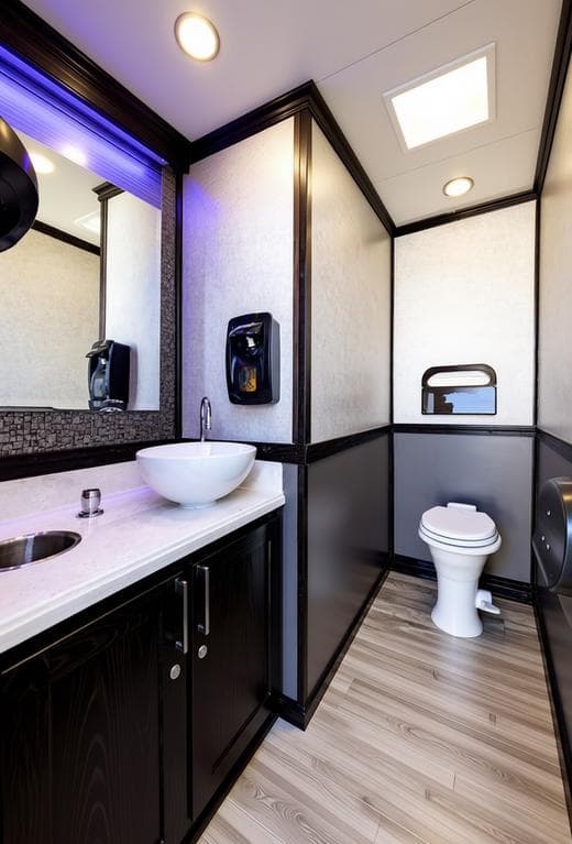 Upscale portable restroom interior with white vessel sink, dark cabinets, and blue LED lighting.